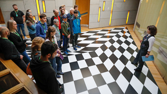 A group of visitors on a guided tour of the Parliament listen to a tour guide in the black and white corridor